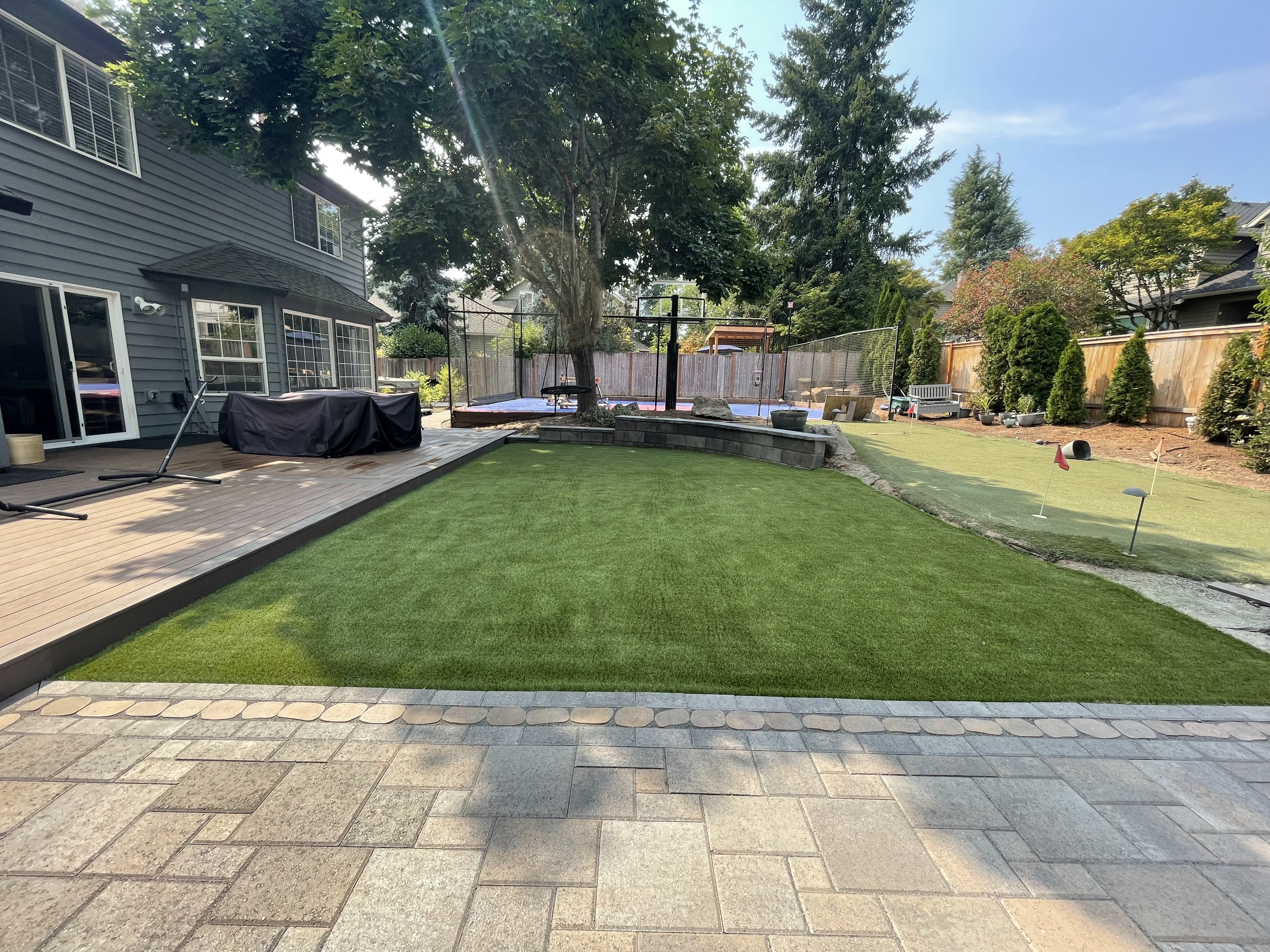 Custom paver patio surrounding a green backyard lawn