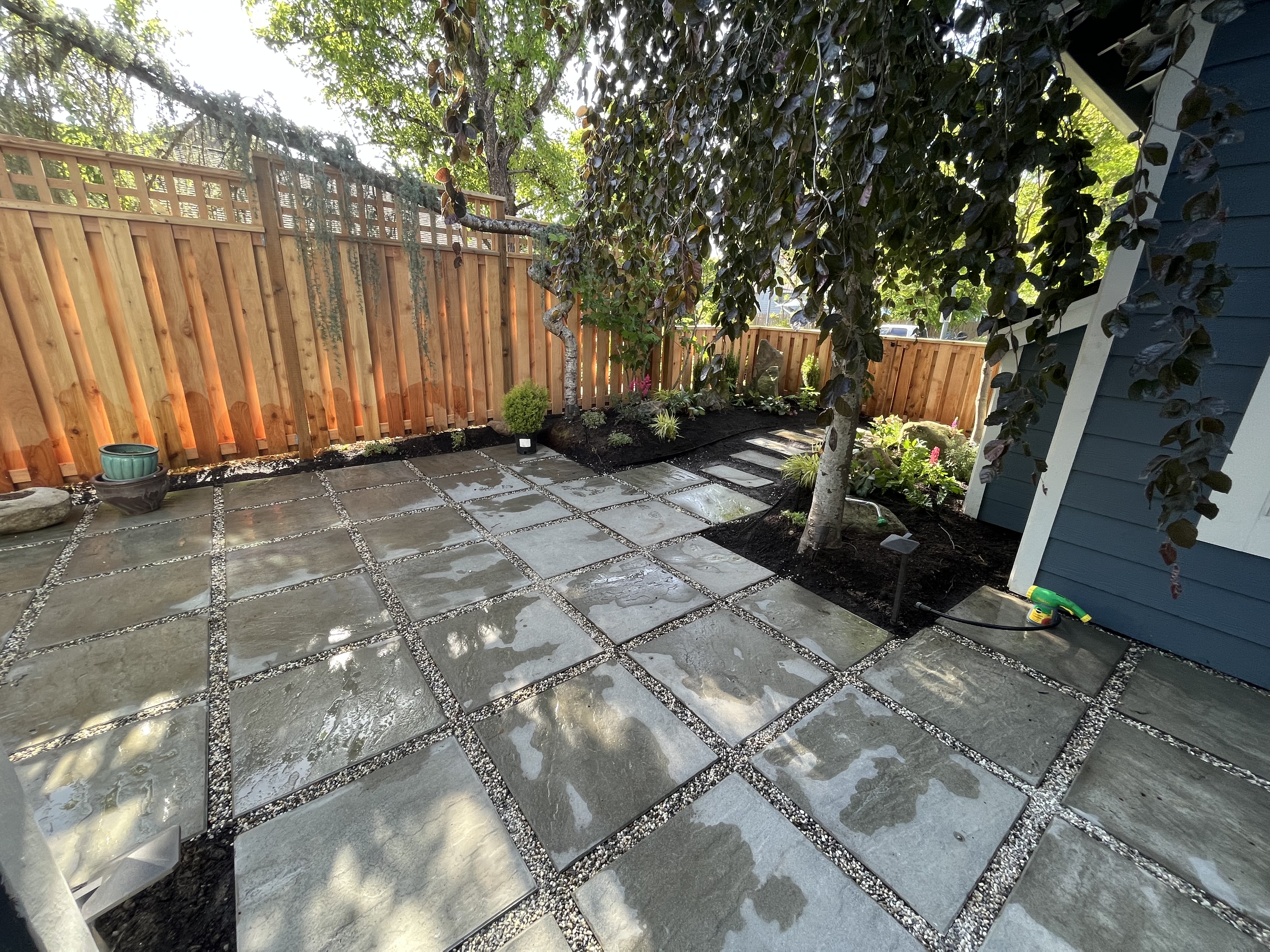 Natural stone patio framed by mature trees and a cedar fence